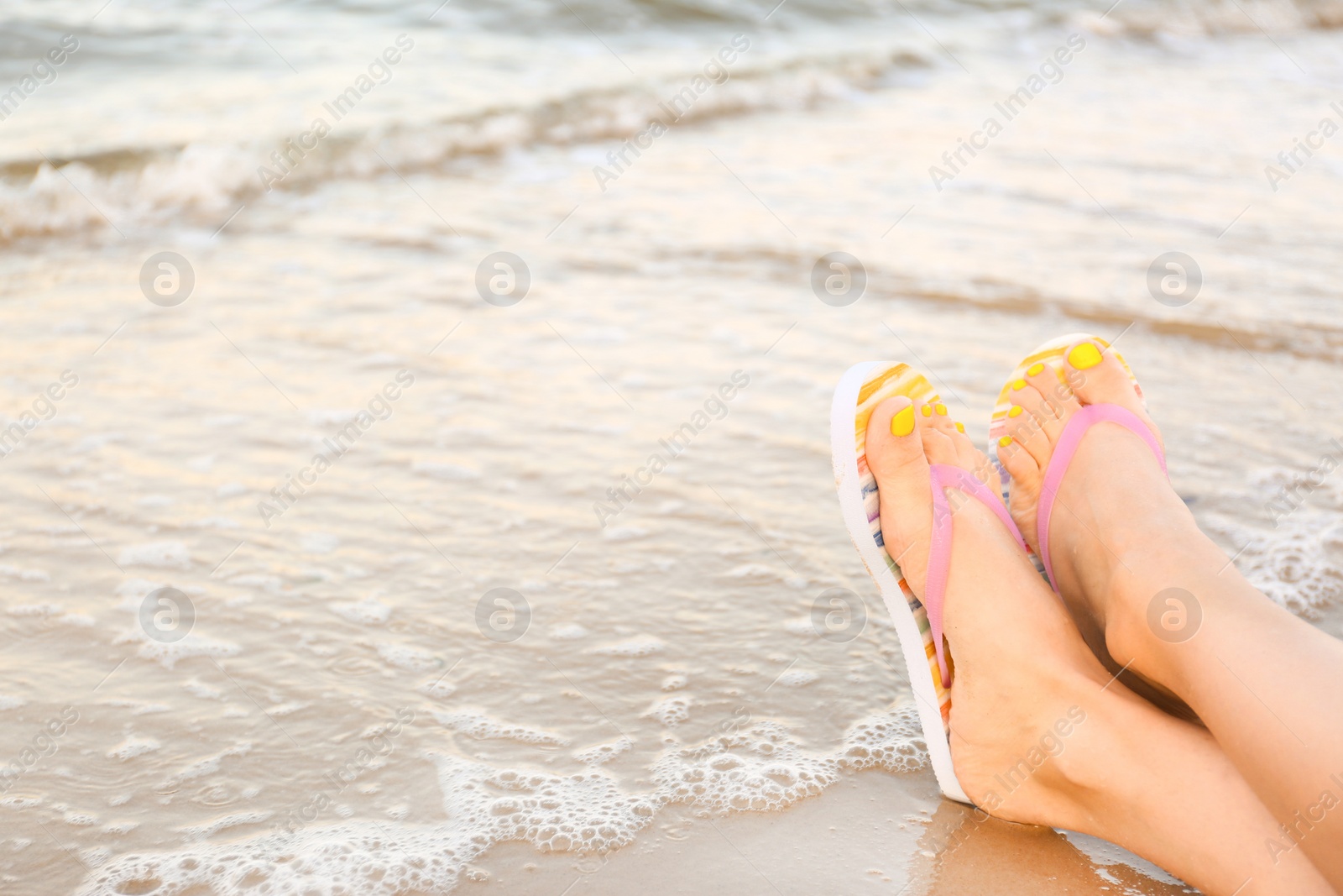 Photo of Closeup of woman with stylish flip flops on sand near sea, space for text. Beach accessories