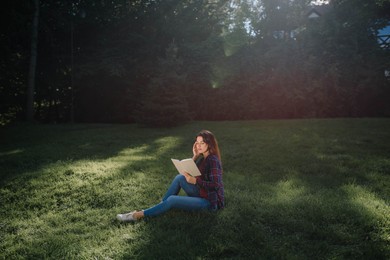 Photo of Young woman reading book in park on sunny day