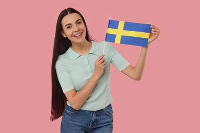 Happy young woman with flag of Sweden on pink background