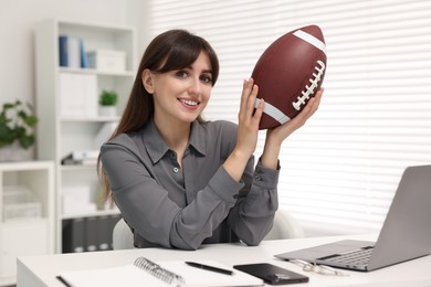 Smiling employee with american football ball at table in office