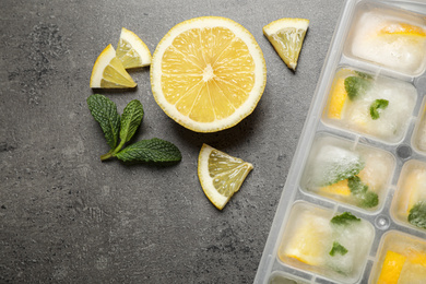 Photo of Ice cubes with lemon and mint in tray on grey table, flat lay