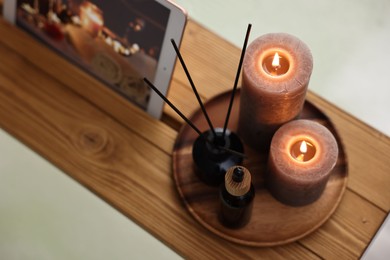 Photo of Wooden tray with tablet, burning candles and aroma products on bathtub, above view