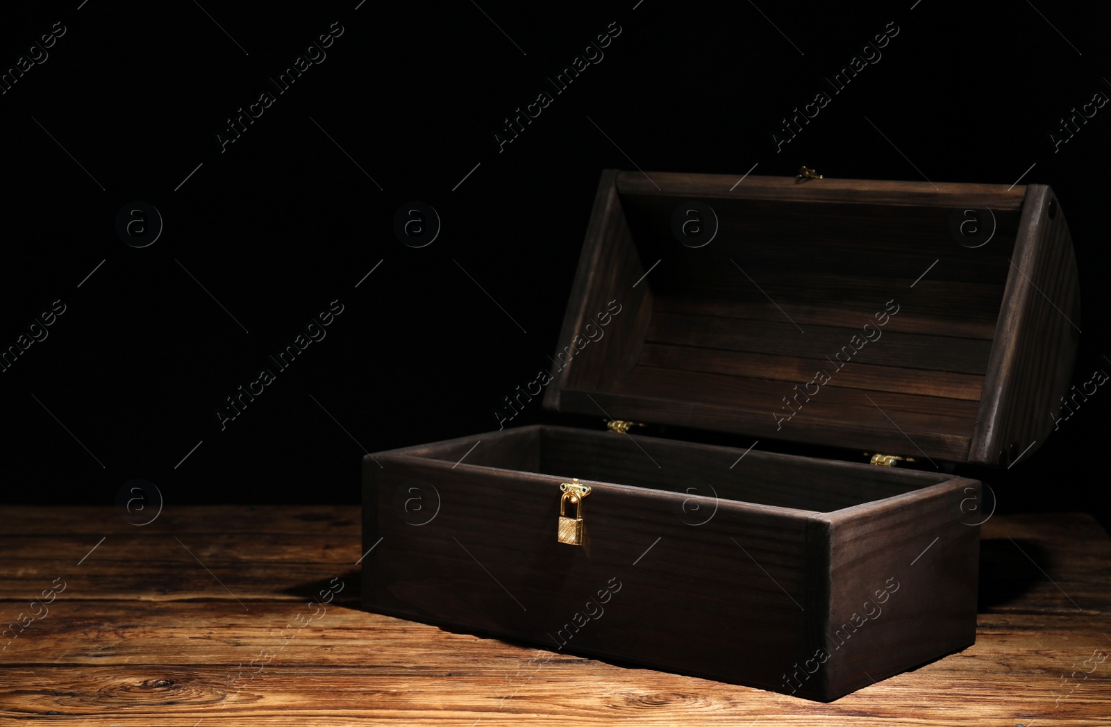 Photo of Empty treasure chest on wooden table against black background. Space for text