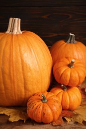 Photo of Pile of ripe pumpkins and dry leaves on wooden table