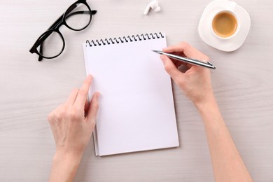 Photo of Woman with notebook and pen at white wooden table, top view. Space for text