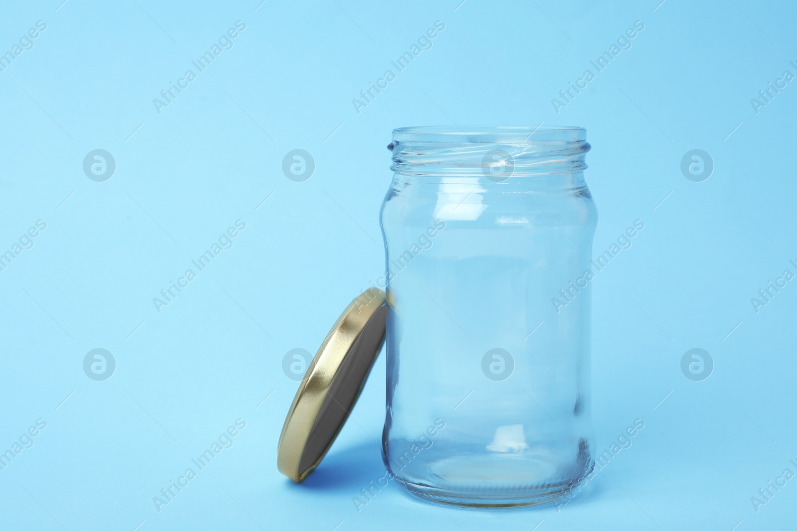 Photo of Open empty glass jar on light blue background, space for text