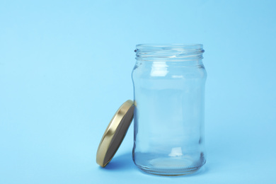 Open empty glass jar on light blue background, space for text