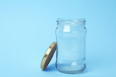 Photo of Open empty glass jar on light blue background, space for text