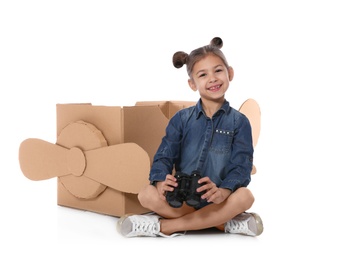 Photo of Cute little girl playing with binoculars and cardboard airplane on white background