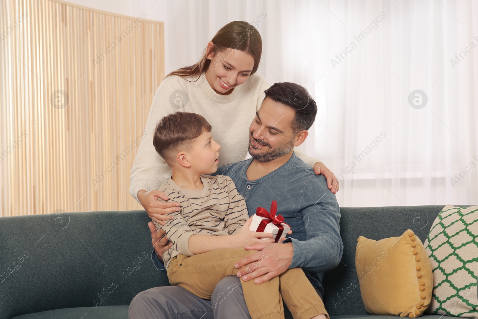Photo of Happy family with gift on sofa at home
