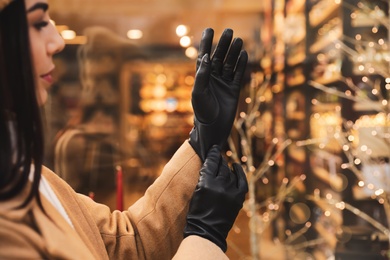 Photo of Woman putting on stylish leather gloves near store decorated for Christmas, closeup