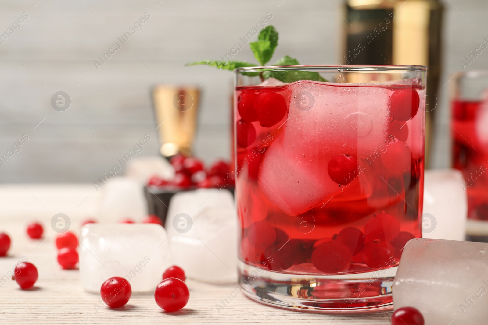 Photo of Tasty cranberry cocktail with ice cubes in glass and fresh berries on wooden table, space for text