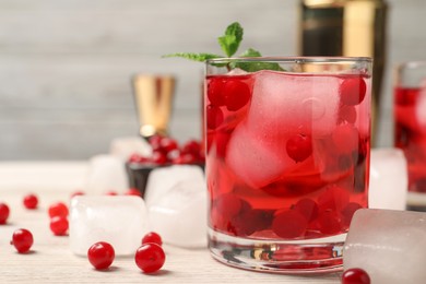 Tasty cranberry cocktail with ice cubes in glass and fresh berries on wooden table, space for text