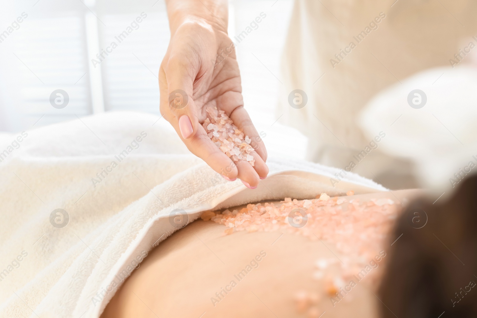 Photo of Young woman having body scrubbing procedure with sea salt in spa salon, closeup