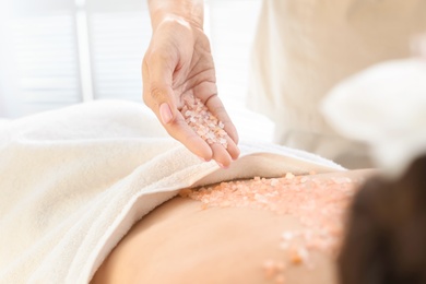 Photo of Young woman having body scrubbing procedure with sea salt in spa salon, closeup