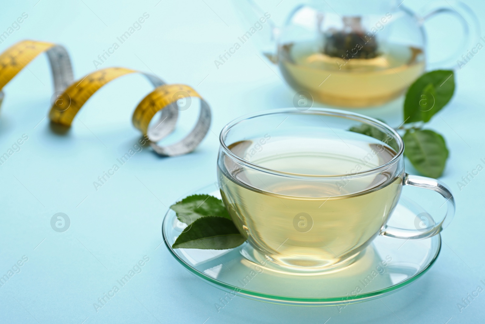 Photo of Glass cup of diet herbal tea and green leaves on light blue background