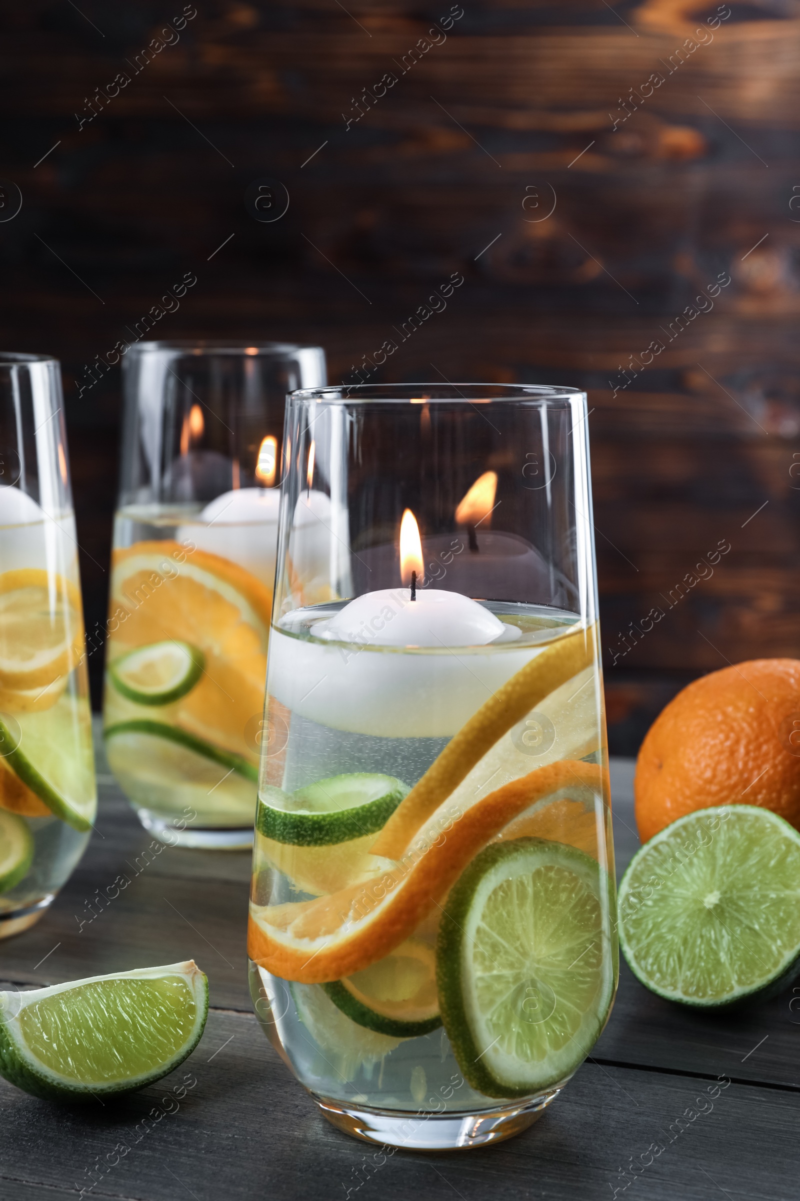 Photo of Candles and fruit slices in glass holders with liquid on wooden table