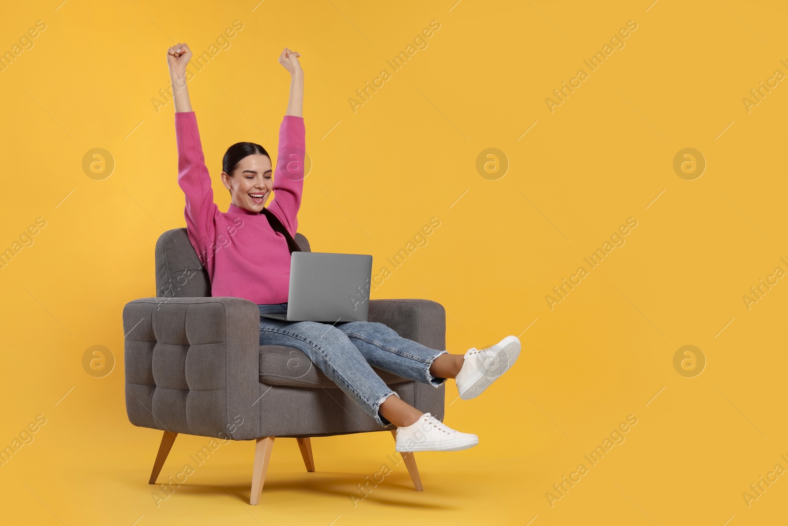 Photo of Cheerful woman with laptop sitting in armchair on orange background