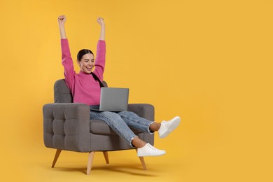 Photo of Cheerful woman with laptop sitting in armchair on orange background