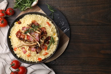 Photo of Bowl of tasty couscous with mushrooms, bacon and tomatoes on wooden table, flat lay. Space for text