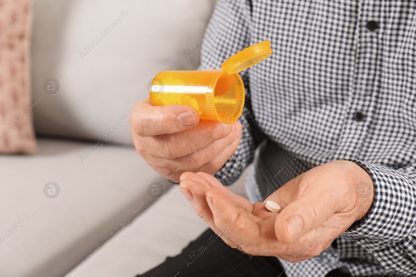 Photo of Senior man pouring pills from bottle into hand indoors, closeup