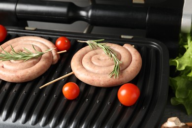 Photo of Electric grill with homemade sausages, rosemary and tomatoes on table, closeup