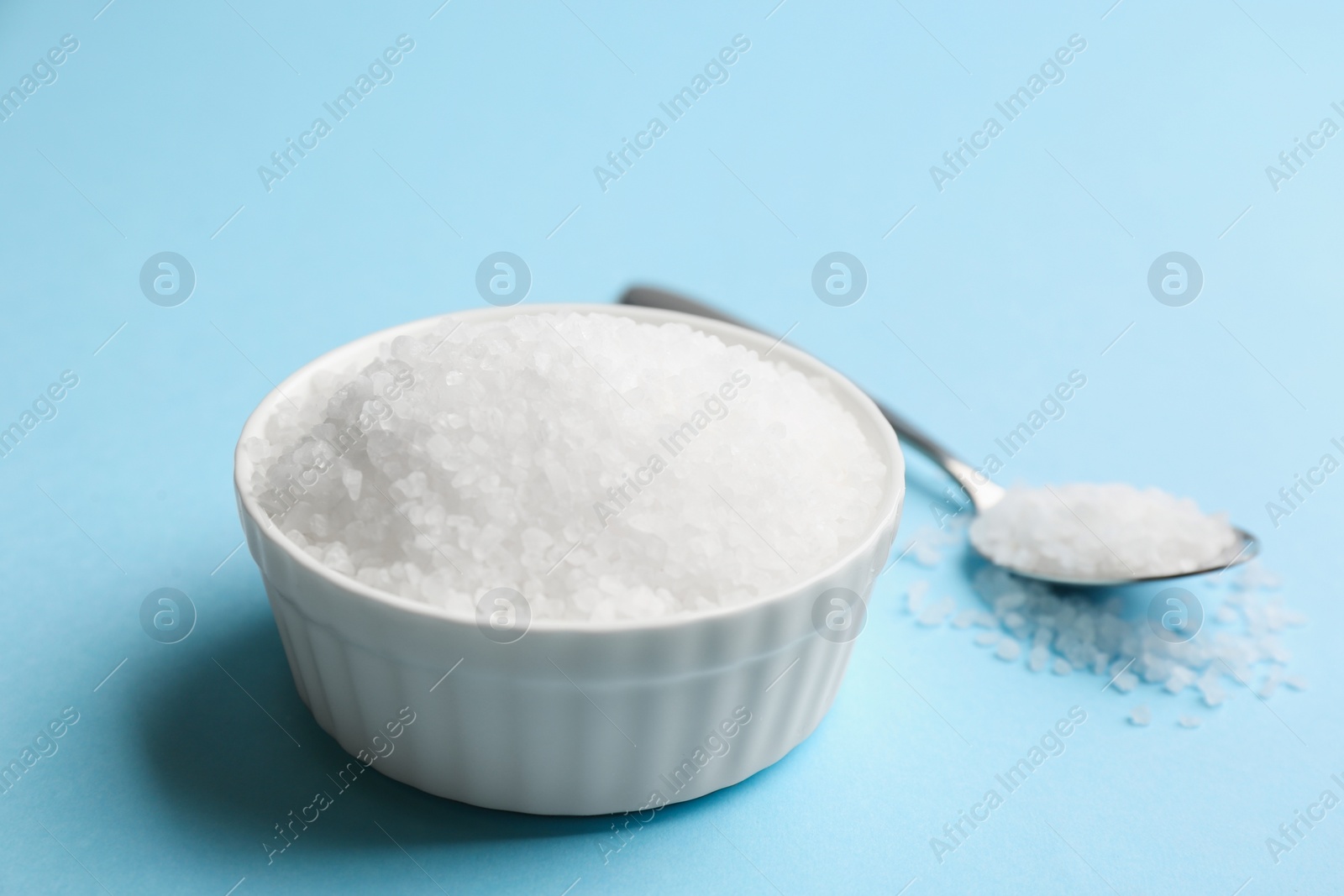 Photo of Bowl and spoon with salt on light blue background, closeup