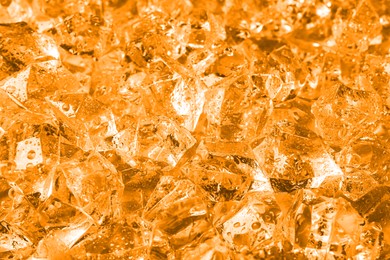 Clear crushed ice as background, closeup view. Toned in orange