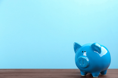 Piggy bank on wooden table against light blue background. Space for text