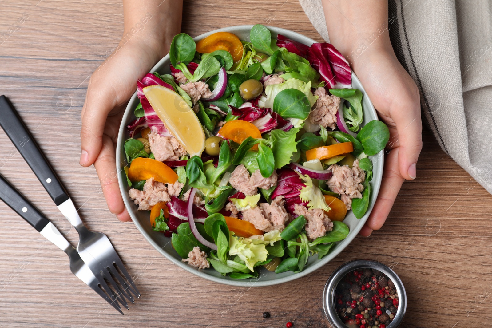 Photo of Woman holding bowl of delicious salad with canned tuna at wooden table, top view