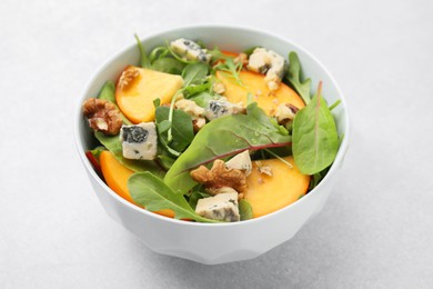 Photo of Tasty salad with persimmon, blue cheese and walnuts served on white table