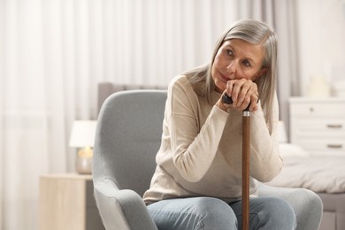 Photo of Mature woman with walking cane in armchair at home