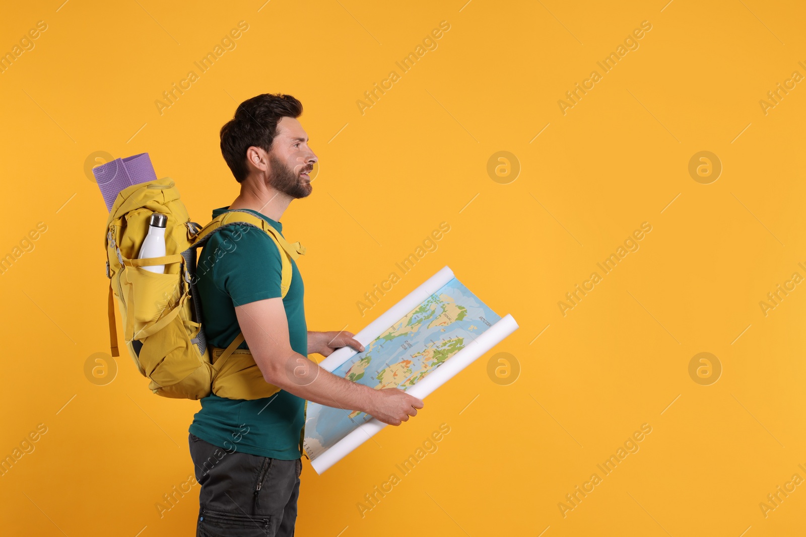 Photo of Happy man with backpack and map on orange background, space for text. Active tourism