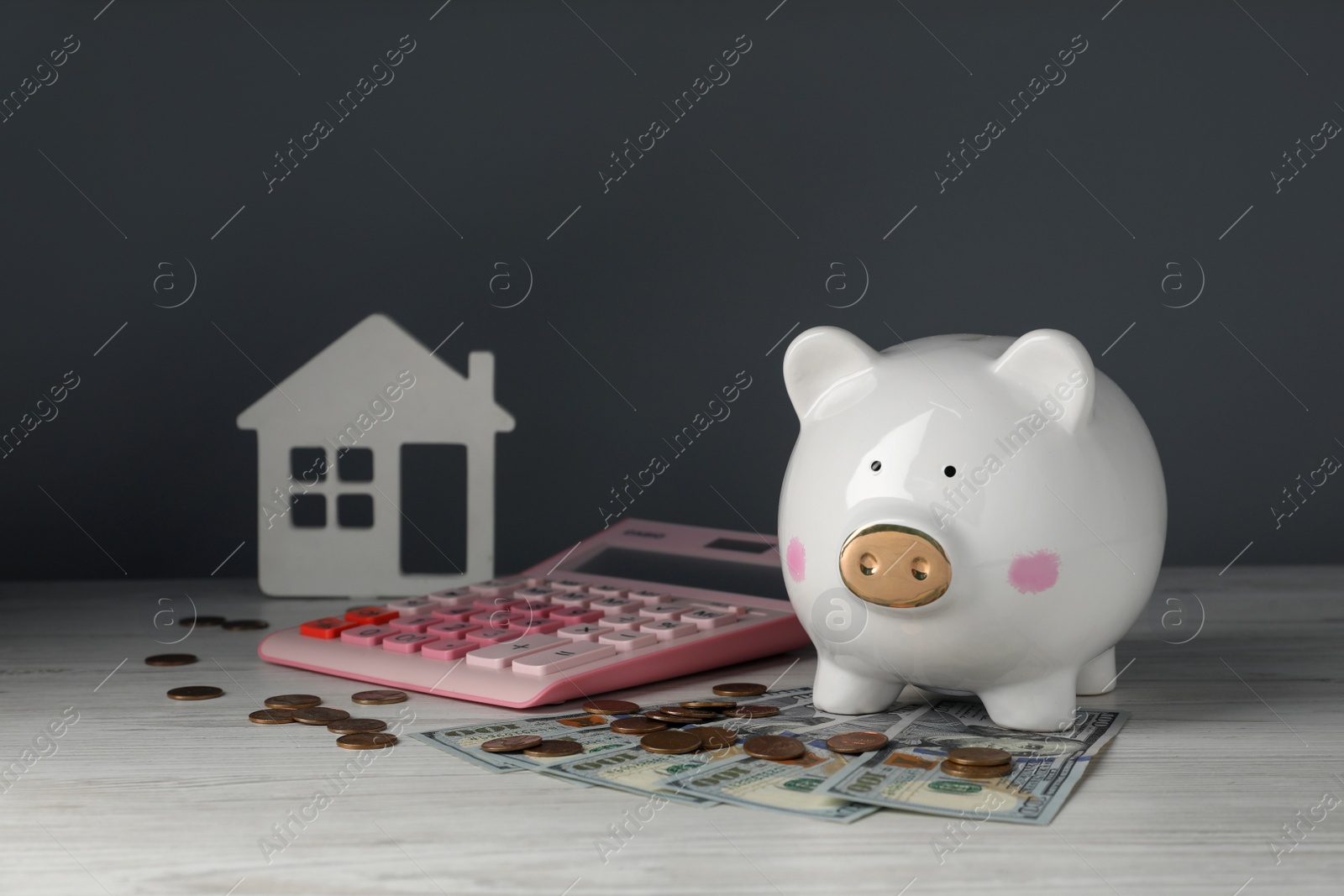 Photo of Piggy bank, house model, calculator and money on white wooden table