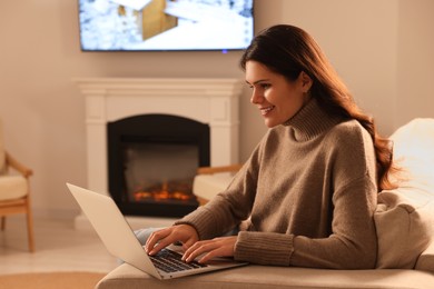 Photo of Young woman working on laptop near fireplace at home