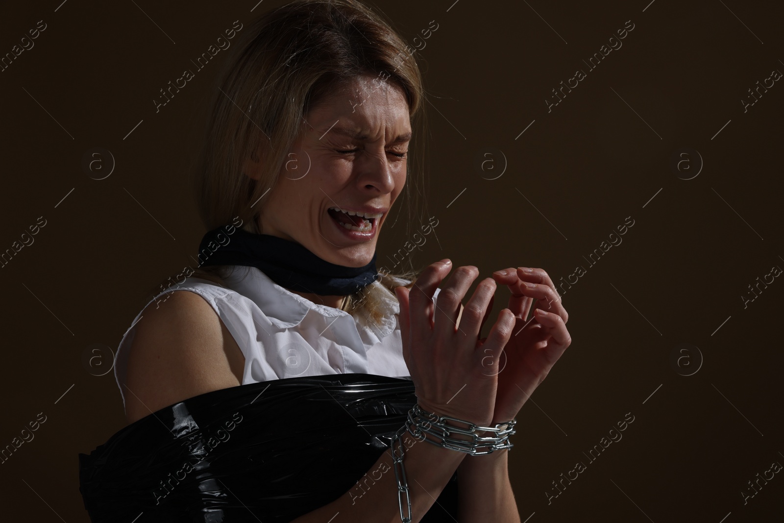 Photo of Scared woman taped up and taken hostage on dark background. Space for text