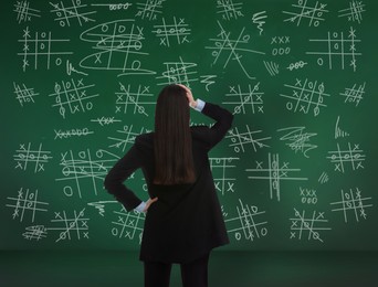 Image of Young businesswoman near green chalkboard with drawn tic tac toe game, back view