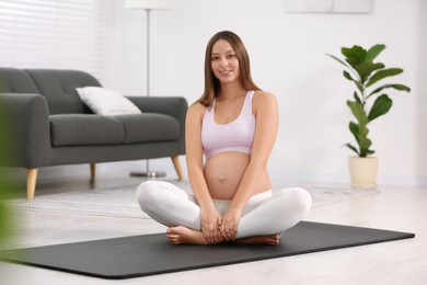 Pregnant woman sitting on yoga mat at home