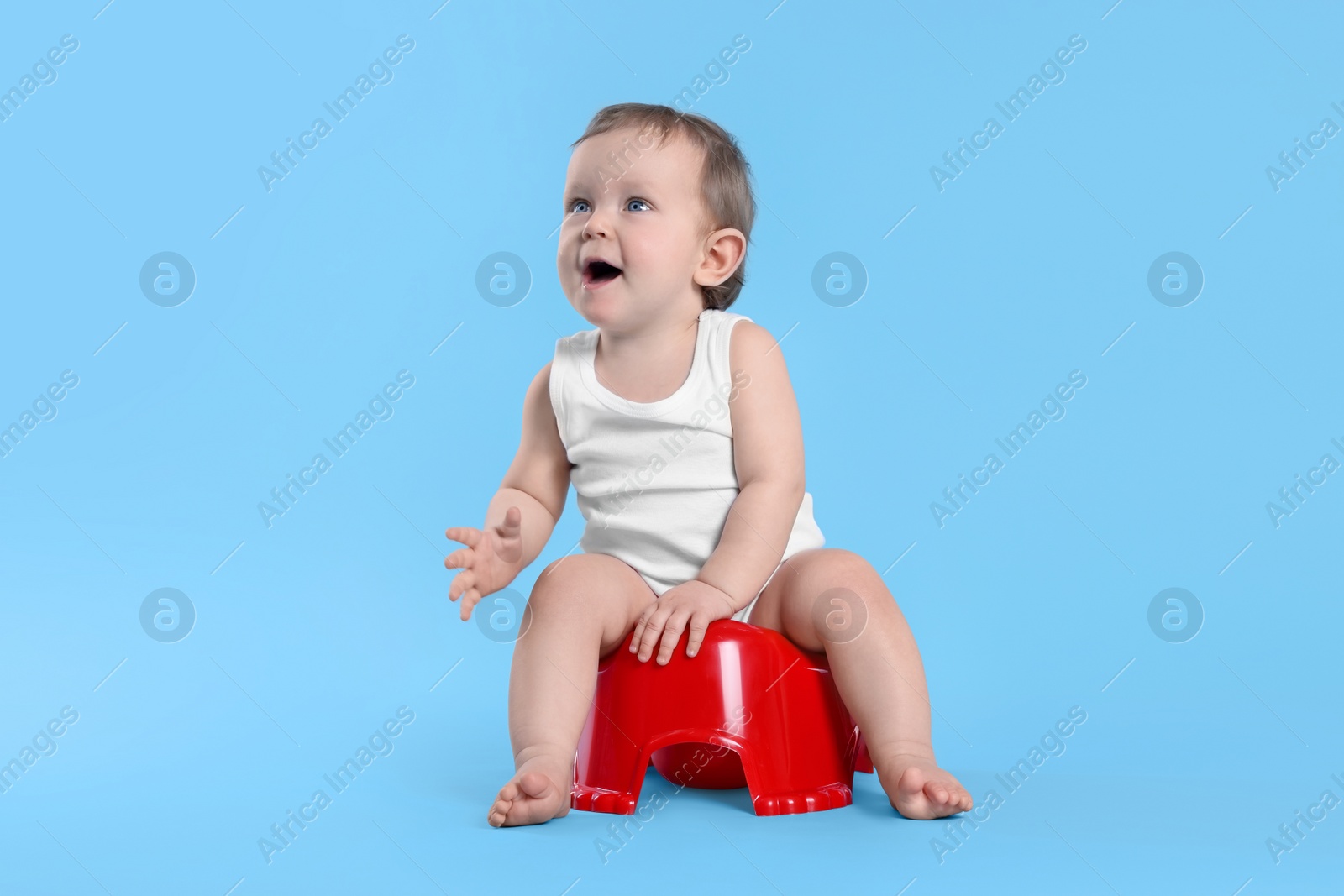 Photo of Little child sitting on baby potty against light blue background. Space for text