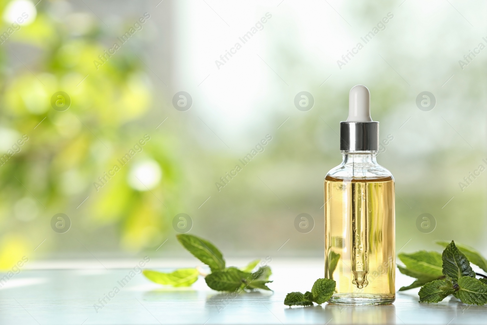 Photo of Bottle of mint essential oil on white wooden table against blurred background. Space for text