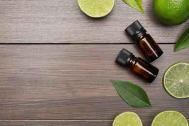 Photo of Bottles of essential oil with lime slices and leaves on wooden table, flat lay. Space for text
