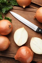 Photo of Whole and cut onions with knife and parsley on wooden table, flat lay