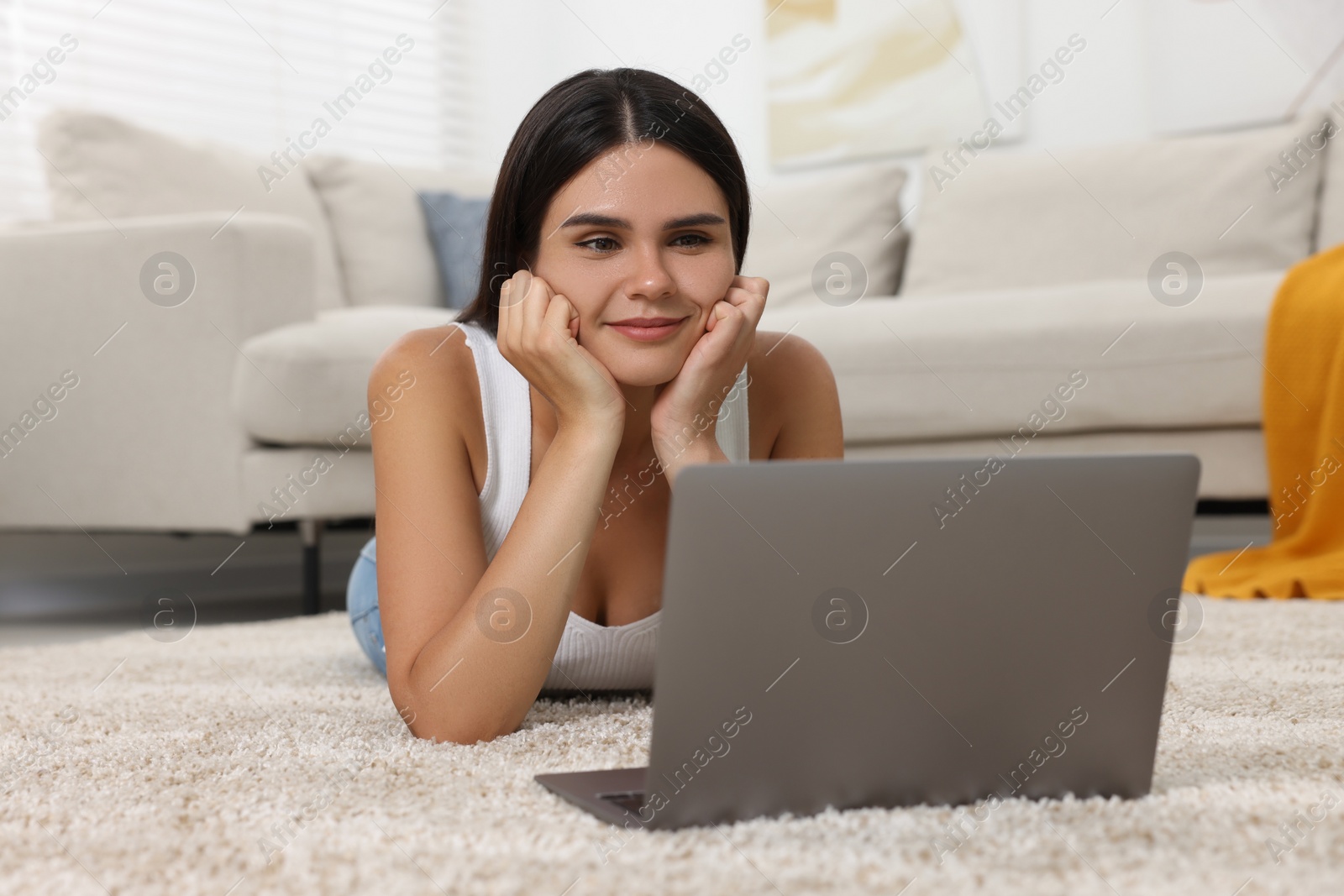 Photo of Happy young woman having video chat via laptop on floor in living room