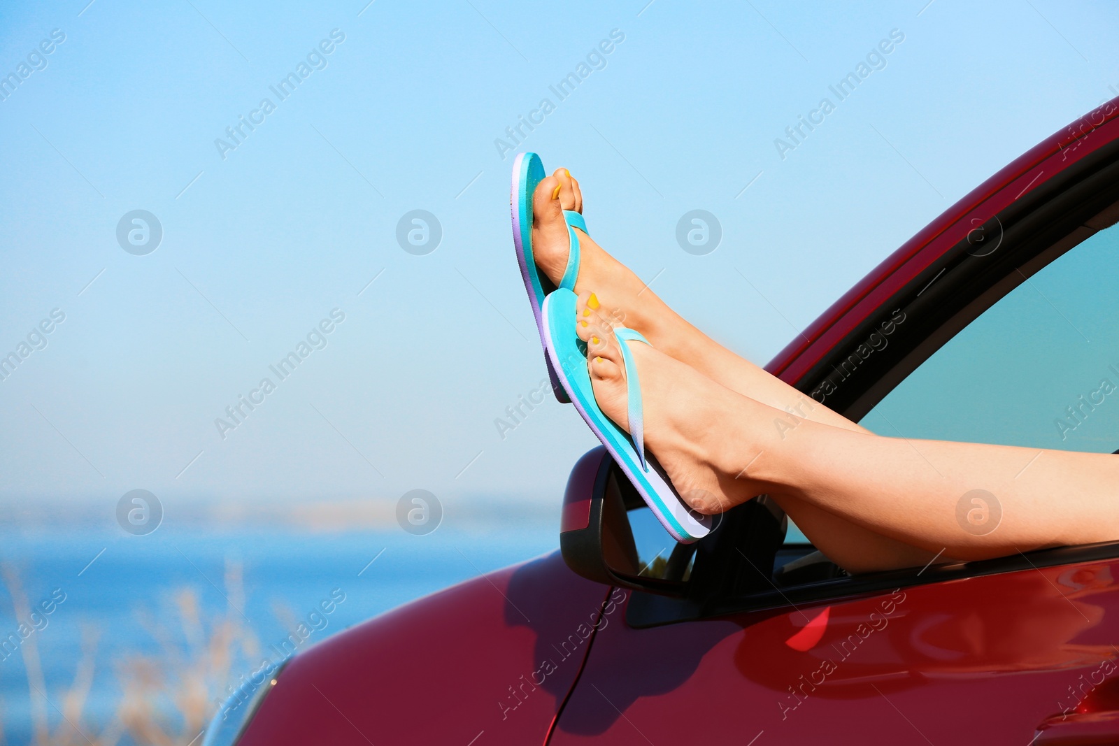 Photo of Closeup of woman showing legs with flip flops from car near sea, space for text. Beach accessories