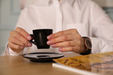 Woman with cup of coffee and magazine at cafe in morning, closeup