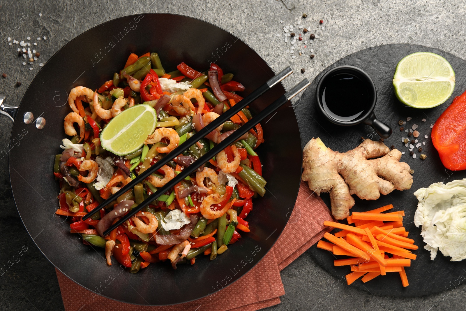 Photo of Shrimp stir fry with vegetables in wok and chopsticks on grey table, flat lay