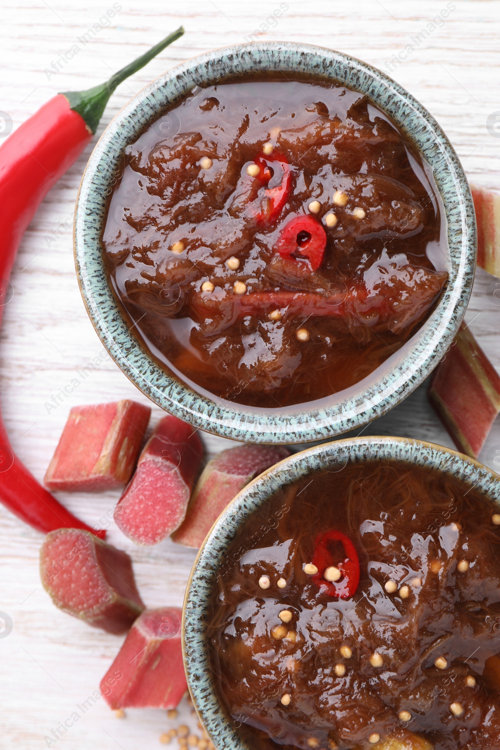 Photo of Tasty rhubarb sauce and ingredients on white wooden table, flat lay