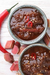 Tasty rhubarb sauce and ingredients on white wooden table, flat lay