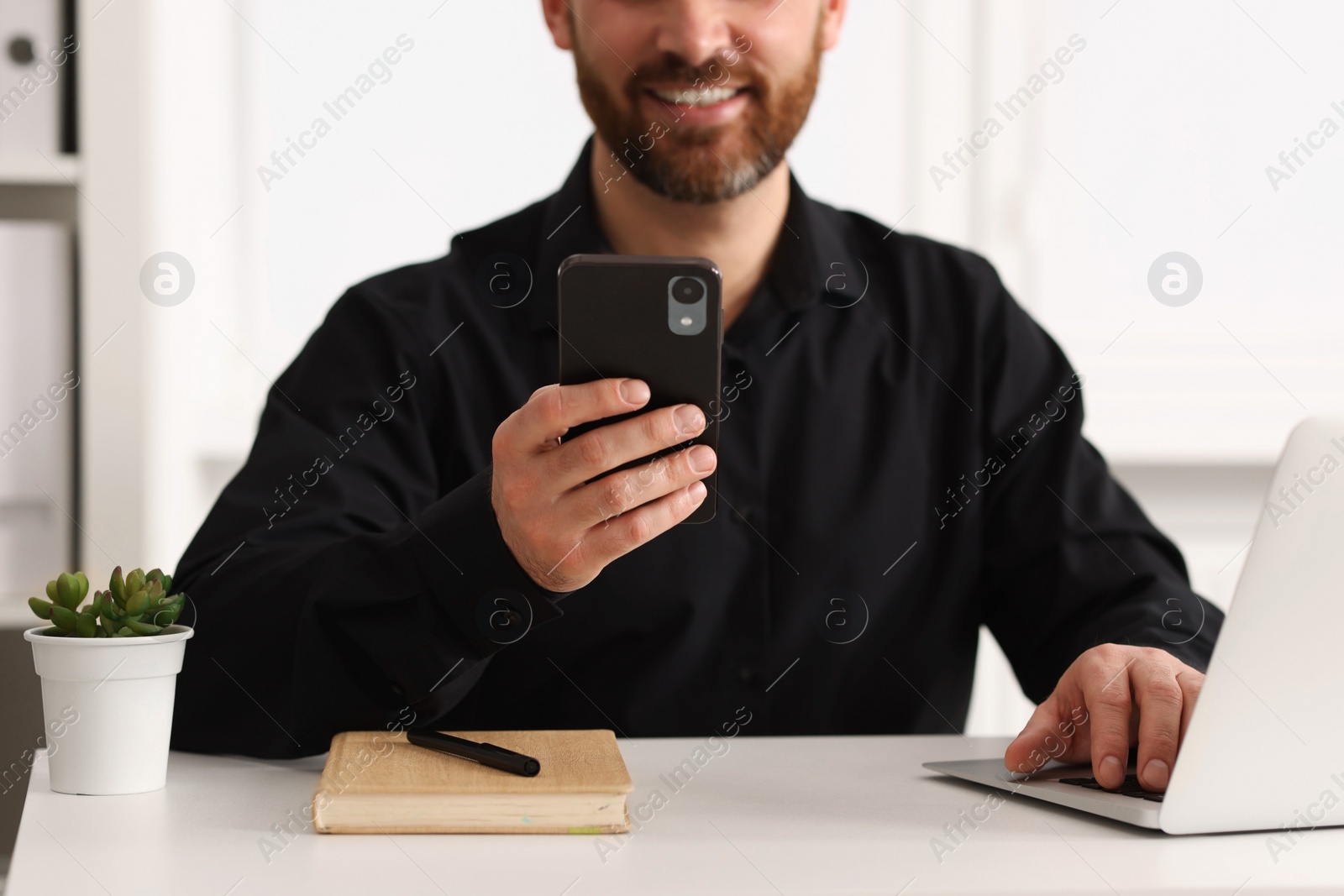 Photo of Smiling man using smartphone at table in office, closeup