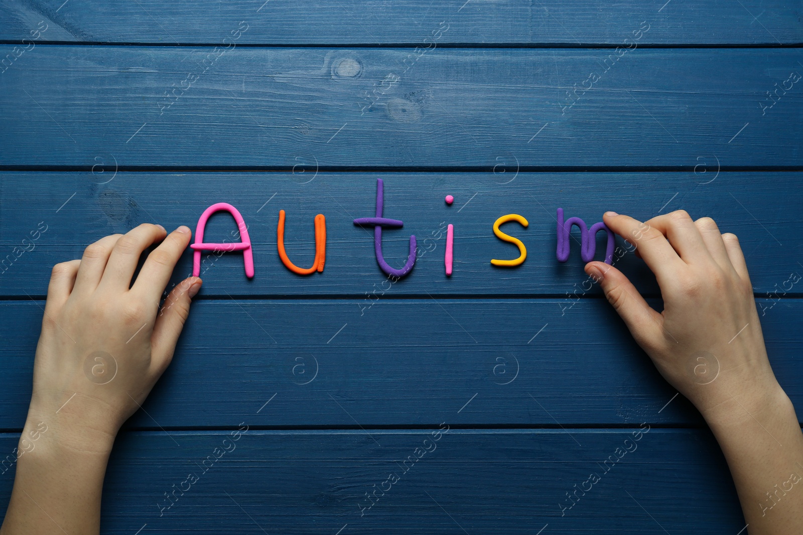 Photo of Woman making word Autism with colorful plasticine on blue wooden table, top view